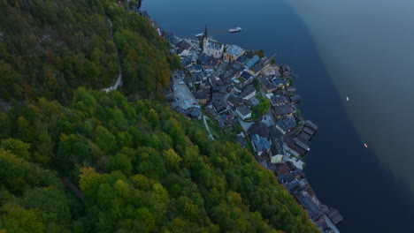 Beautiful-descending-aerial-shot-of-Hallstatt-small-remote-Austrian-town-in-valley-between-rocky-mountains-next-to-a-deep-lake