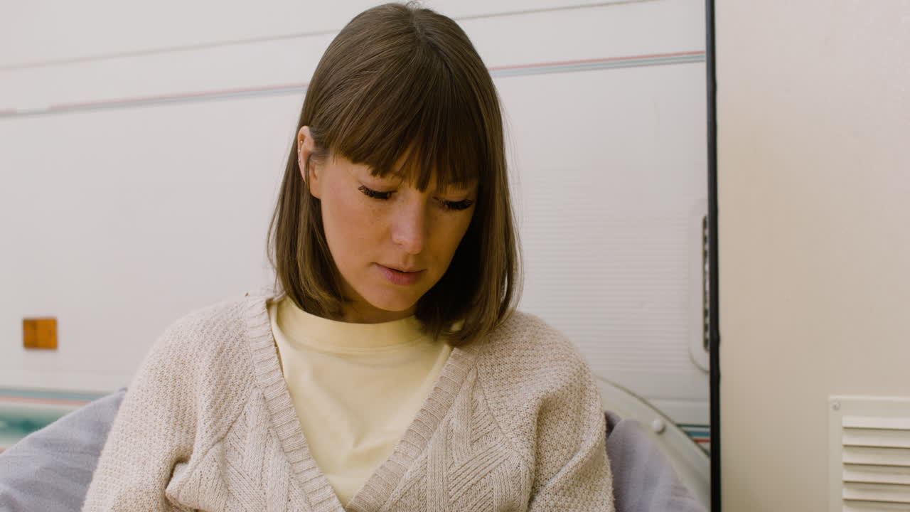 mujer concentrada leyendo un libro mientras se sienta en una silla cerca de una autocaravana en el bosque