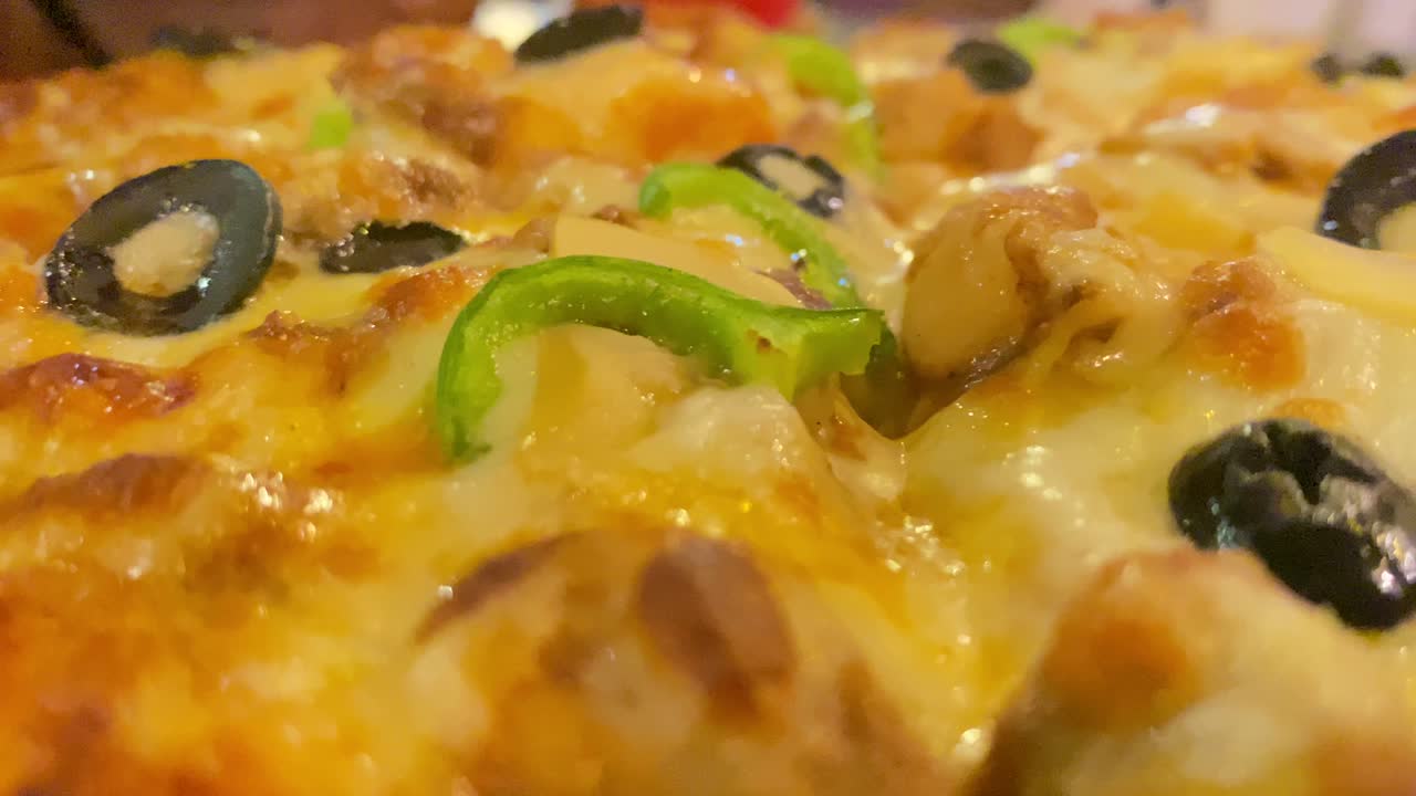 acérquese a esta deliciosa pizza con queso derretido, coloridos pimientos y sabrosas aceitunas en este delicioso video de primer plano