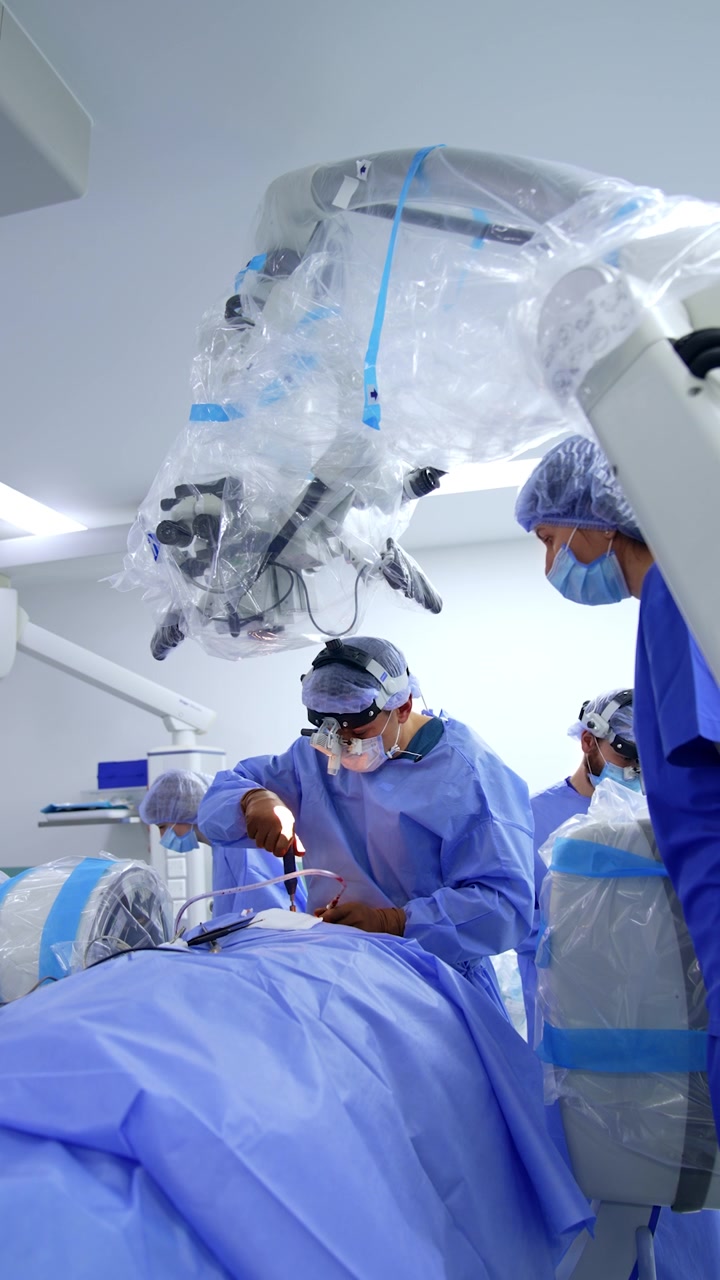 Mandlig kirurg opererer patienten under det medicinske mikroskop. Lægen anvender et skruetrækkerværktøj under operationen. Vertikal video.