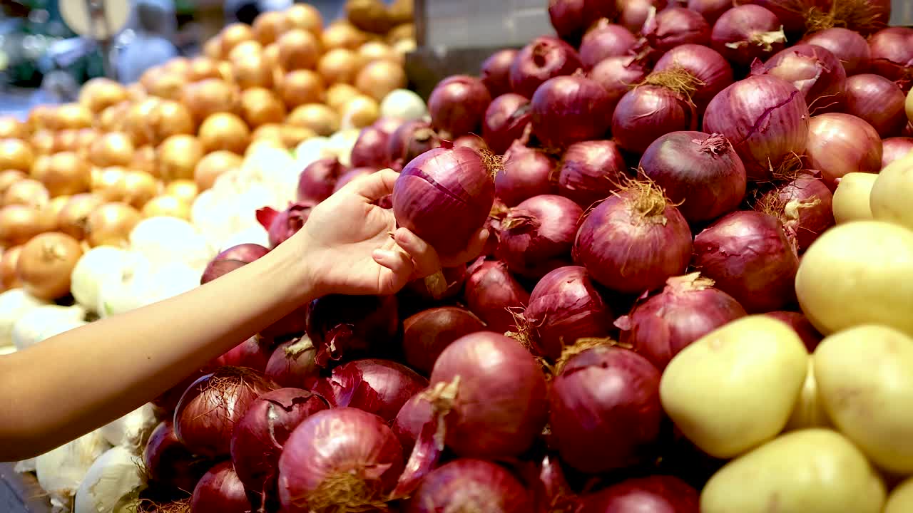 A shopper's hand selects red onions from a vibrant produce display under bright supermarket lighting