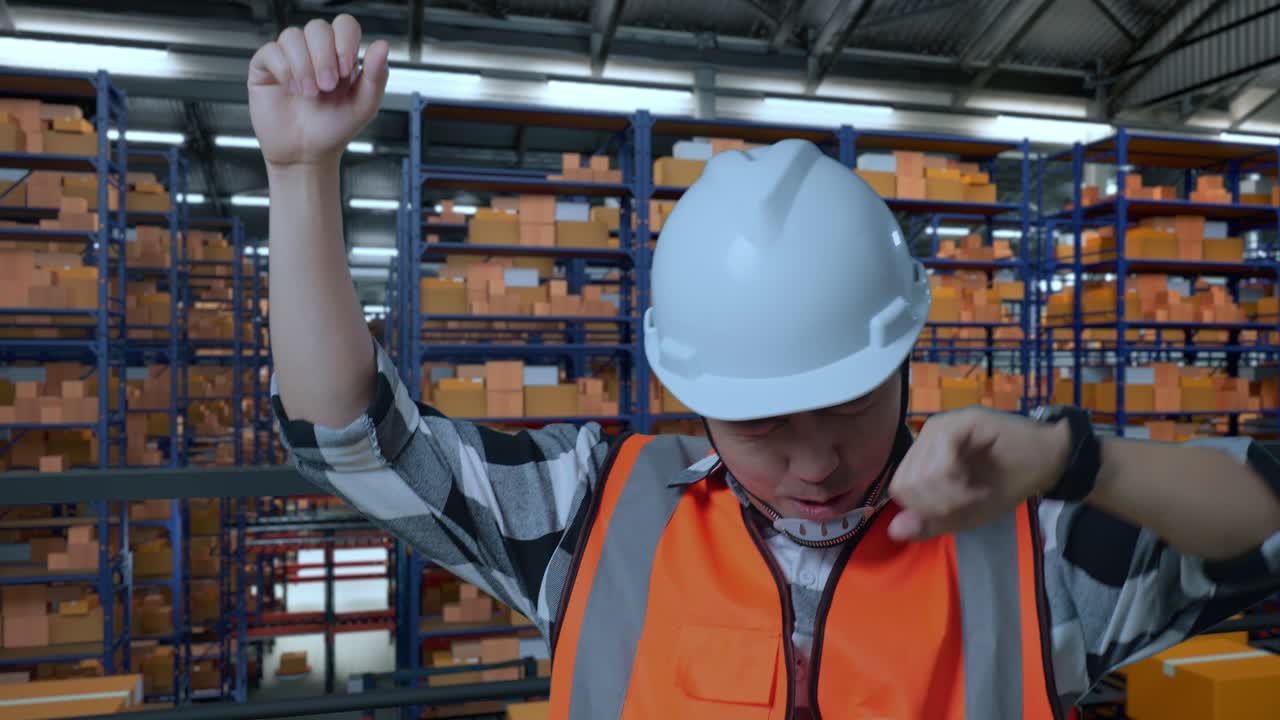 primer plano de ingeniero masculino asiático con casco de seguridad gritando gol y bailando celebrando mientras estaba de pie en el almacén con estantes llenos de mercancías de entrega