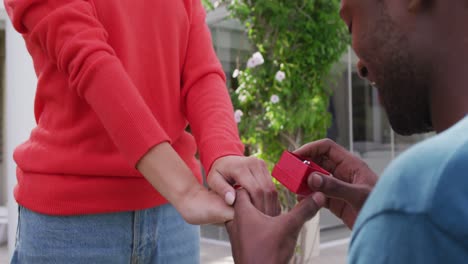 midsection of biracial man proposing to woman on knees with box with ring