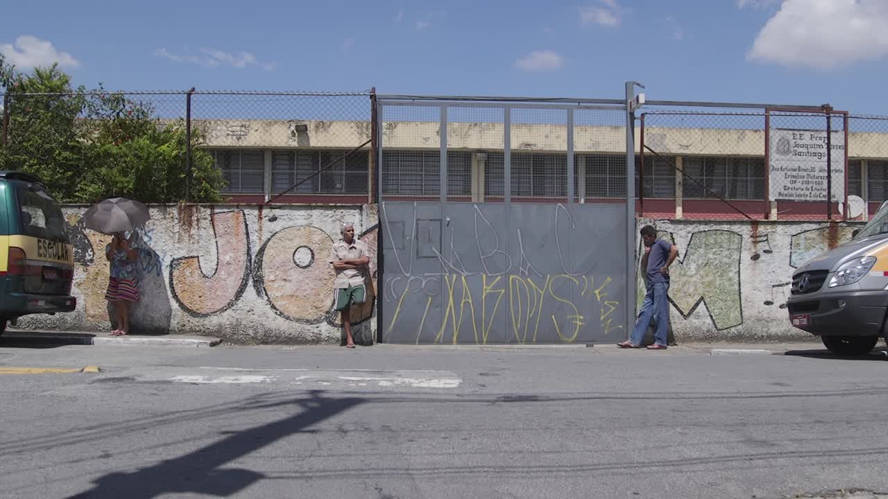 Urban street scene with graffiti on a wall and people near a school gate