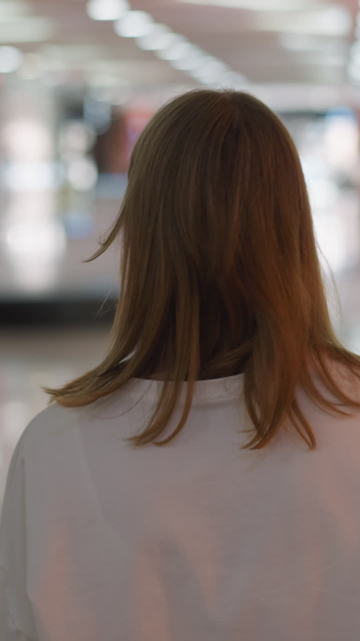 화려한 불빛과 유리 요소를 특징으로하는 흐릿한 배경으로 둘러싸인 쇼핑몰을 걸어다니는 색 을 입은 여자의 뒷면