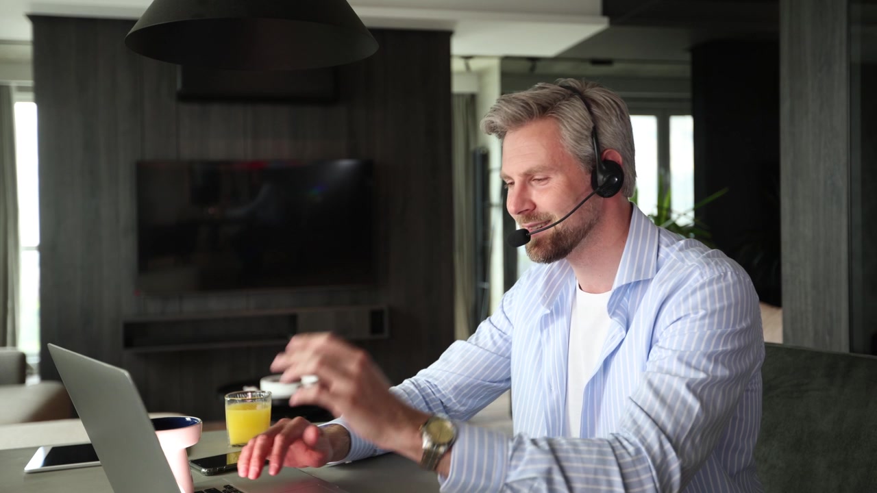 Midaldrende mand med headset arbejder på bærbar computer under videoopkald