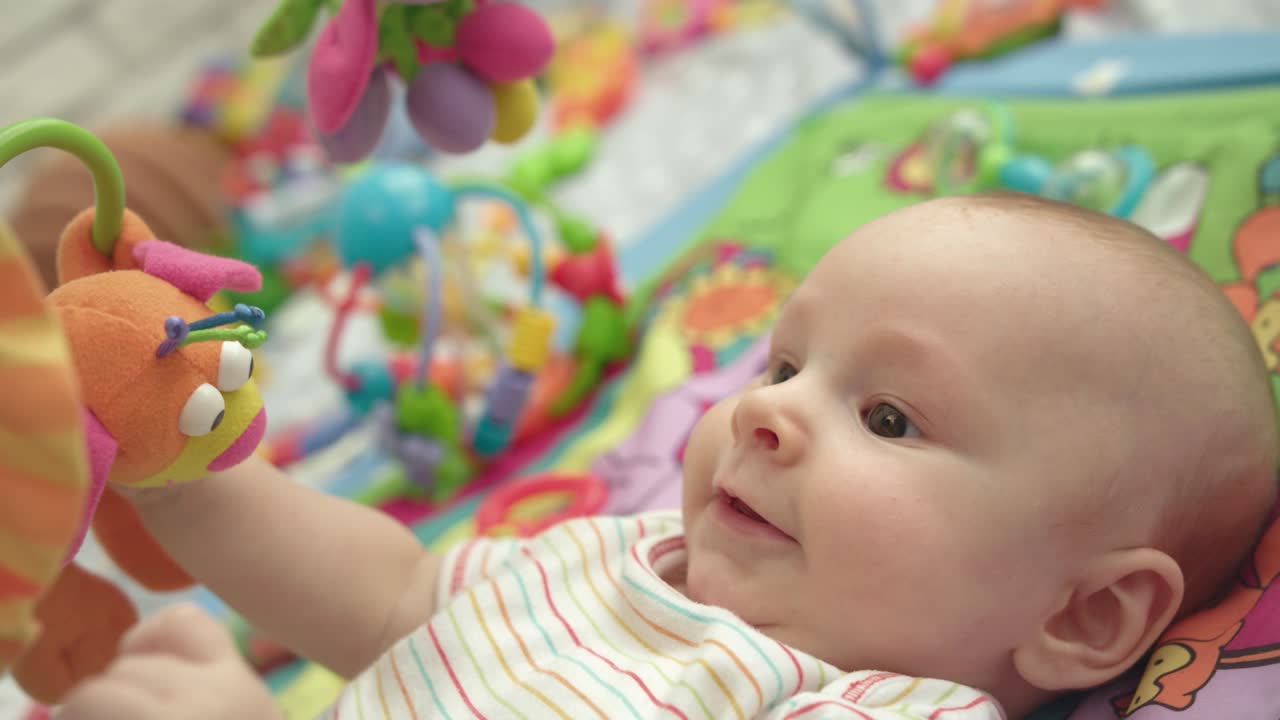 Cute infant have fun with toys. Close up of happy baby lying on developing mat