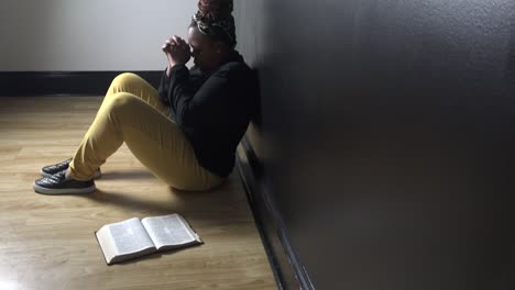 Black-woman-sitting-alone-praying-to-God-with-bible-lying-next-to-her-as-she-prays