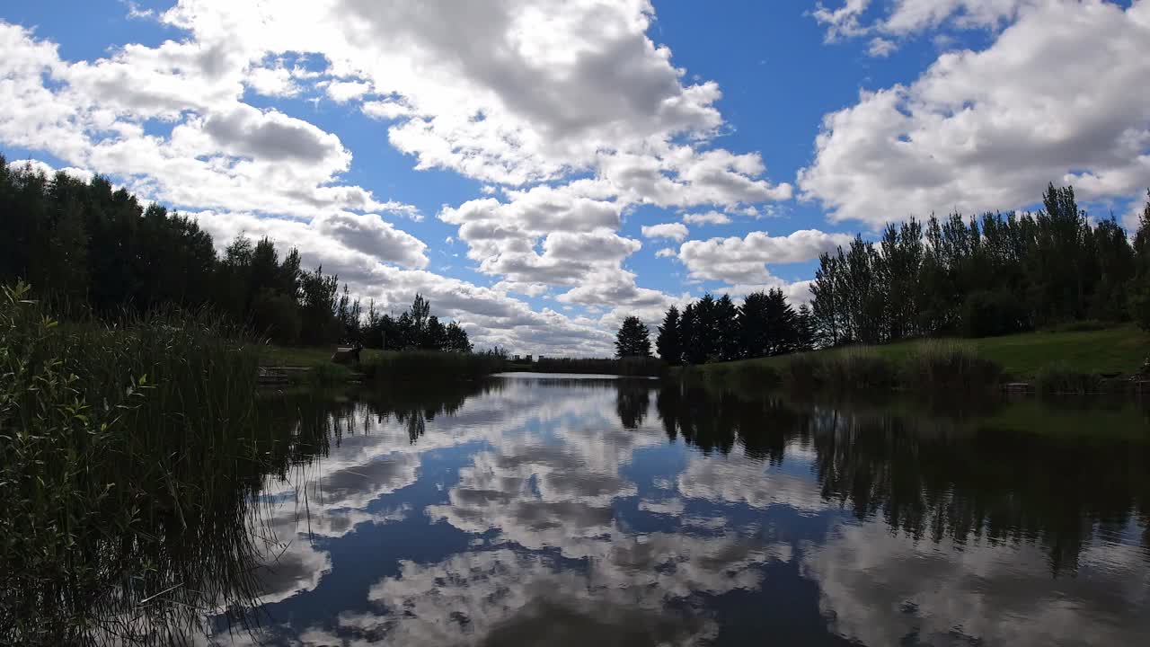 Vibrant scenic blue lake water mirror reflection of bright clouds and trees in sky