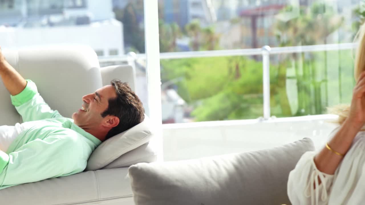 mujer joven hablando en el teléfono móvil mientras el hombre usando la tableta digital en el fondo en casa