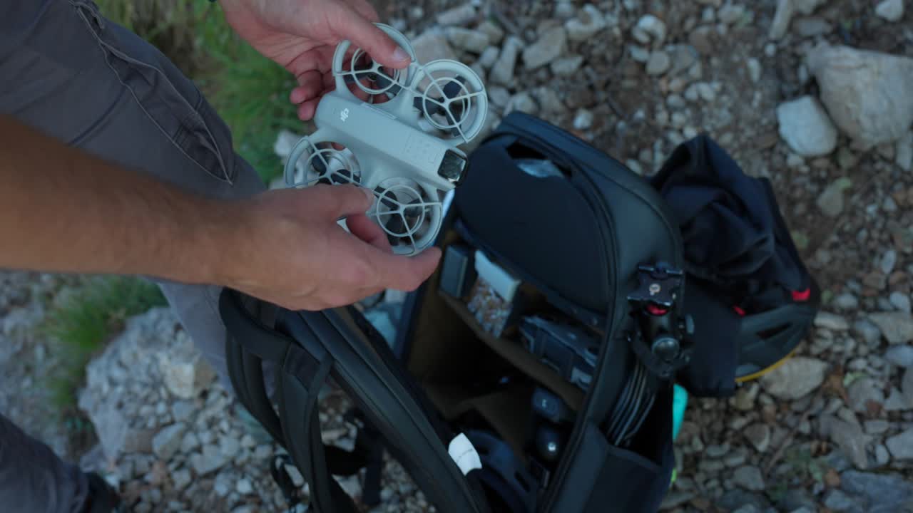 A drone operator prepares for flight by taking equipment from a camera backpack on rocky ground, focusing on outdoor exploration and technology.