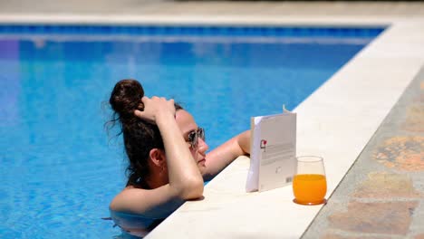 Una-Mujer-Está-Leyendo-Un-Libro-Junto-A-La-Piscina