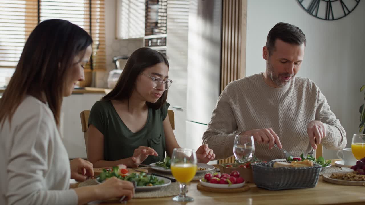 세 명 의 백인 가족 이 함께 아침 식사 를 나누고 있다