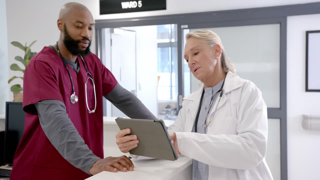 Diverse male and female doctors in discussion using tablet in hospital reception, slow motion
