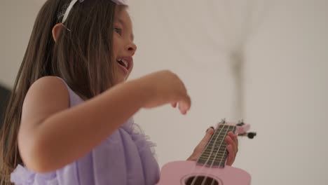 a beautiful little girl is playing the ukulele in the living room for her mom.