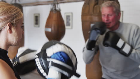 senior male boxer with younger female coach in gym using training gloves