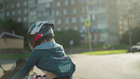 a lady rides a power bike on a sunny day with her helmet on, her checkered shirt fluttering in the wind, the sun reflects off her back as she moves through an urban environment