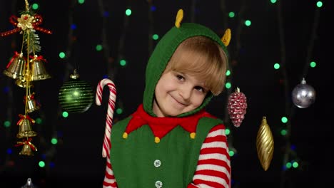 teen kid girl in christmas elf santa claus helper costume showing thumbs up on black background