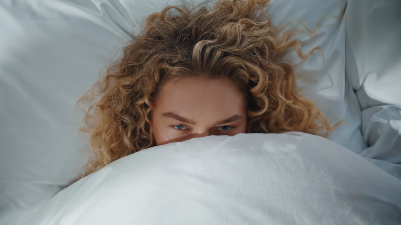 Playful woman hiding blanket in bed closeup. Relaxed blonde enjoying morning