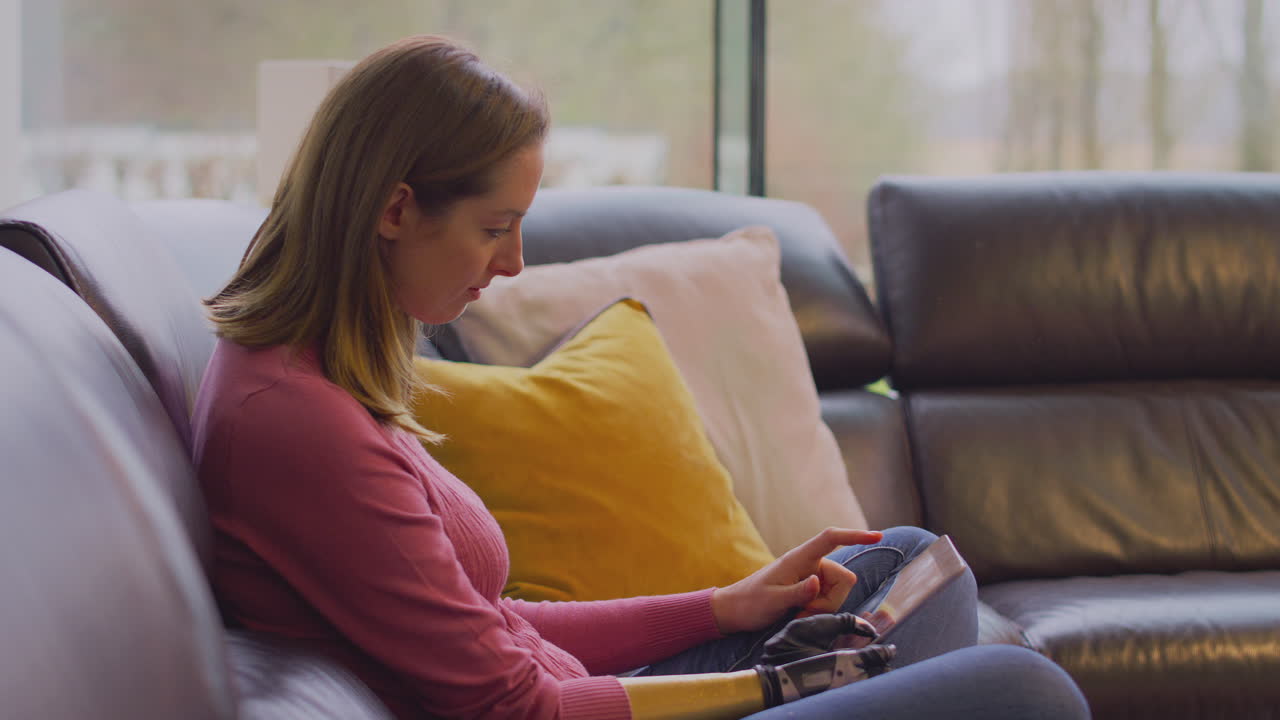 Woman With Prosthetic Arm And Hand At Home Using Digital Tablet