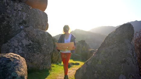 Cheerful-young-woman-reading-map-amidst-rocky-formations-during-hiking-trip