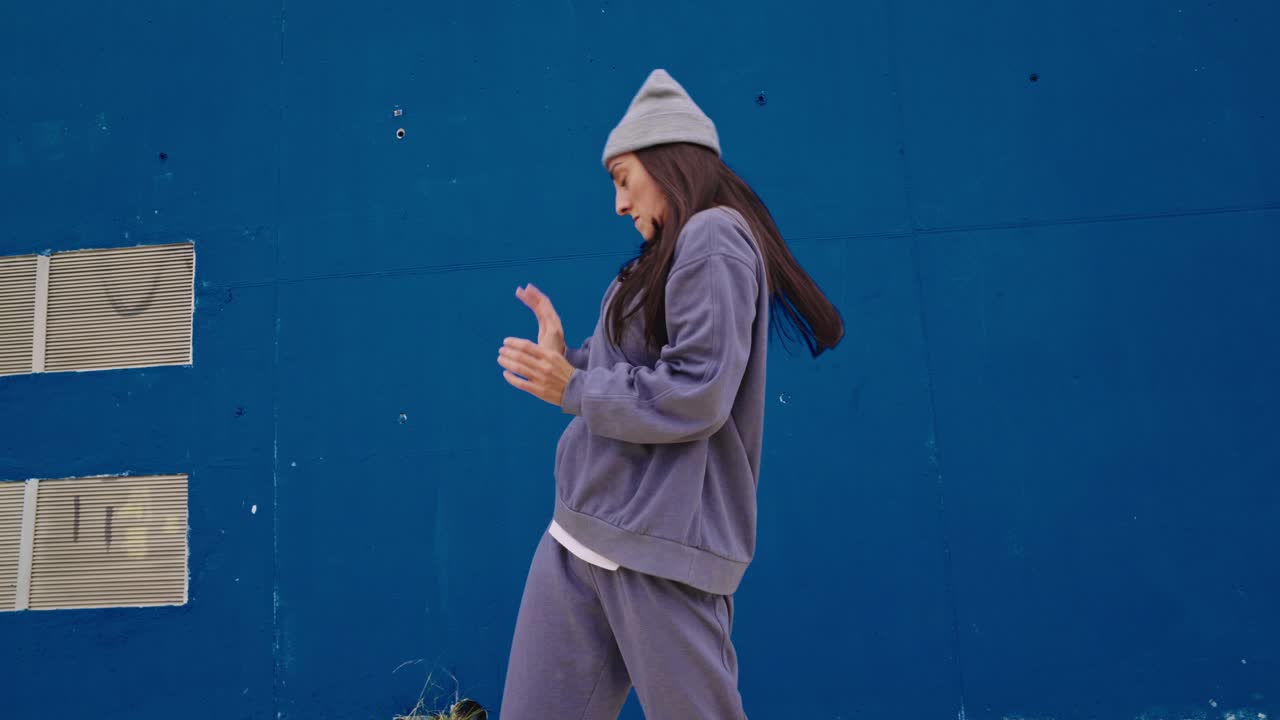 Woman in streetwear dancing against a blue wall
