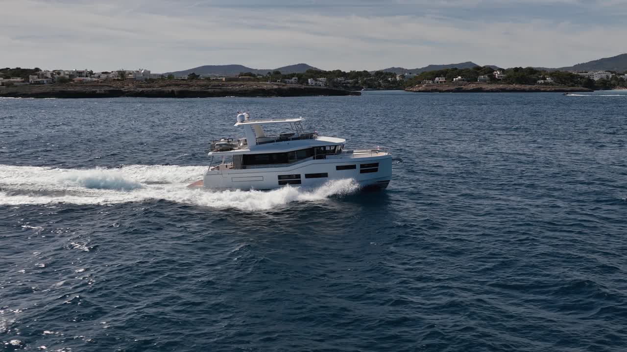 Beautiful boat driving at sea with cliff with houses in the background in slow motion filmed by drone