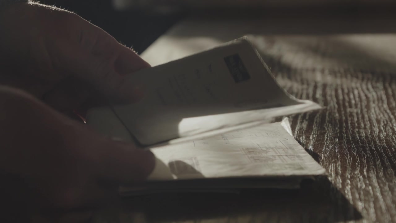 Person sorts through brown stamped envelopes on a dark table in dramatic low light, suggesting retro financial correspondence and payment demands.