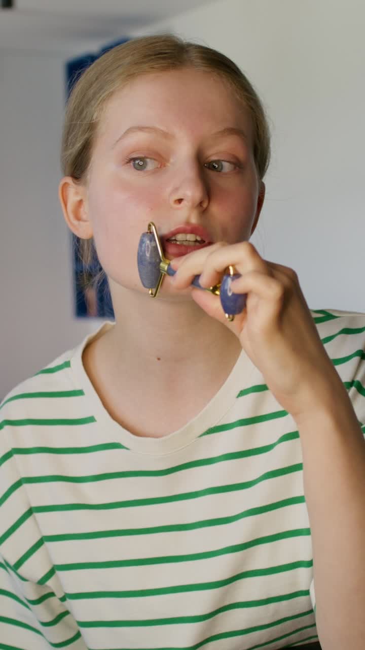 una adolescente usando un rodillo de jade para un masaje facial