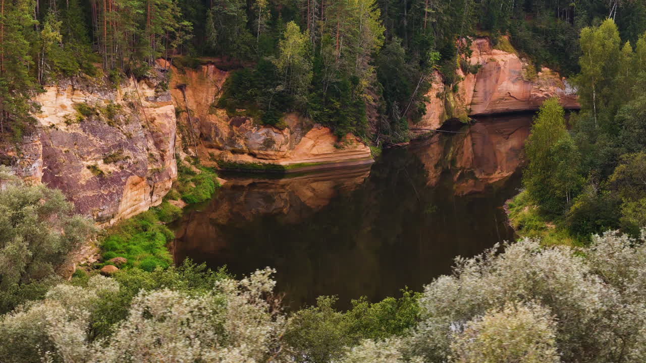 Kauniit punaiset hiekkakivikalliot (Erglu Cliffs) heijastuen Gaujan kansallispuiston muinaisista joista, metsistä ja laaksoista, Latvia; suosittu matkailukohde Baltian Euroopassa