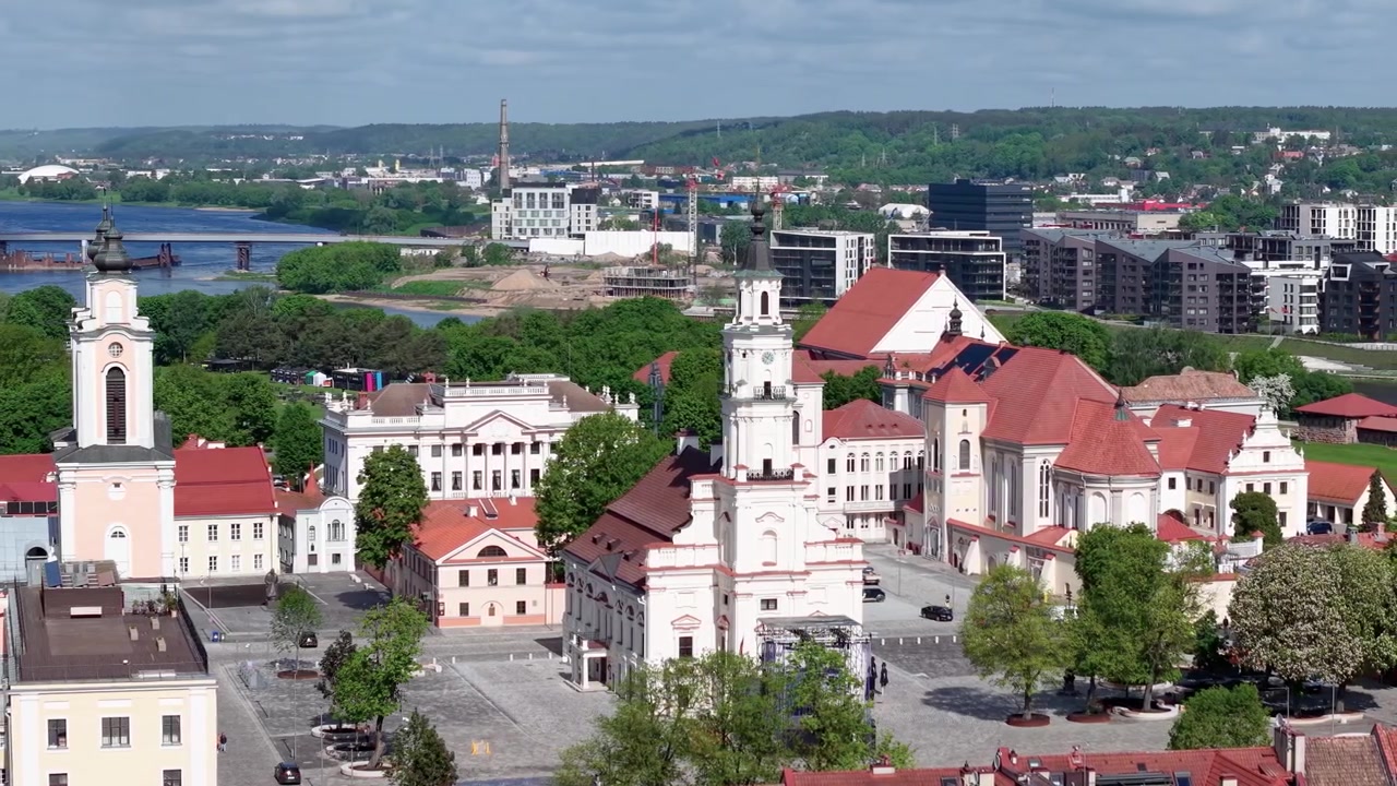Ohromující letecké záběry ukazují Náměstí radnice v Kaunasu, historické barokní budovy, červené střechy a svěží zeleň za jasného denního světla. Ostré, široké panoramatické video z dronu