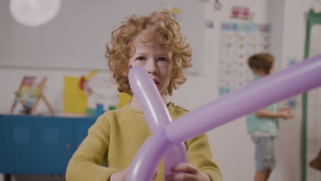 front view of little boy looking at camera and playing with a purple sword shaped balloon