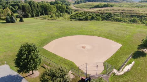 Rising-aerial-of-baseball-diamond-in-the-rural-countryside,-trees-and-fields-in-distance