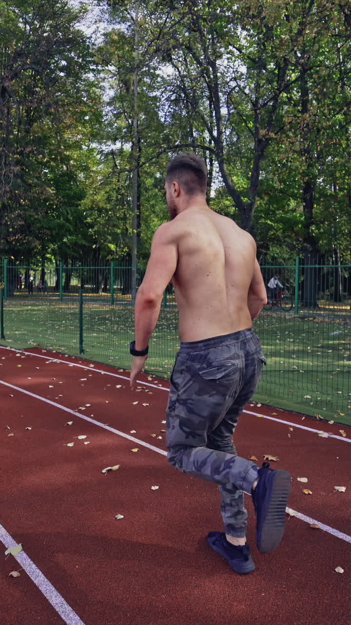 Male sprinter training for race. Back view of athlete without shirt starting running at outdoor athletics track and field stadium. Sport and fitness concept. Vertical video