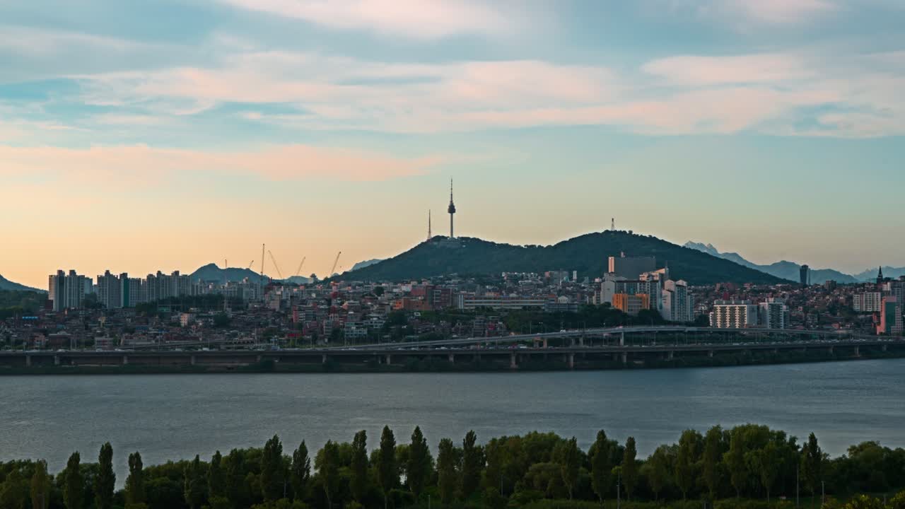 Aerial real-time view of Seoul's Namsan Tower and Han River Park at sunset with soft colorful clouds in the sky above the city skyline