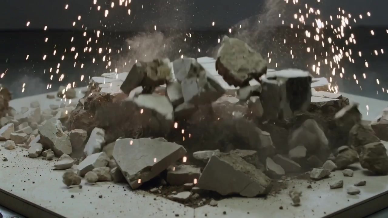 Sparking square slab ejecting fragments on low pedestal in studio, metal rod initiating dust