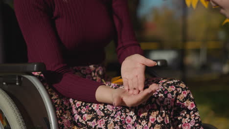 una mujer joven se sienta en silla de ruedas mirando a la mariquita en la palma