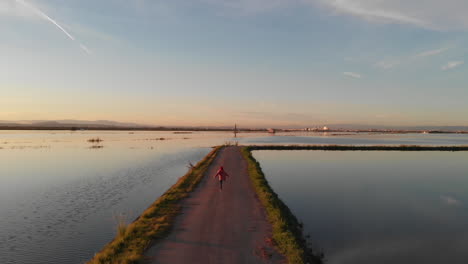 aerial view following. beautiful sunset over the rice field covered with water. perfectly smooth surface of water in albufera national park, valencia spain. happy young girl running and jumping
