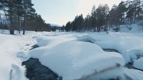 mountain river and landscape covered in massive layer of snow in norway, aerial fpv fly backward view