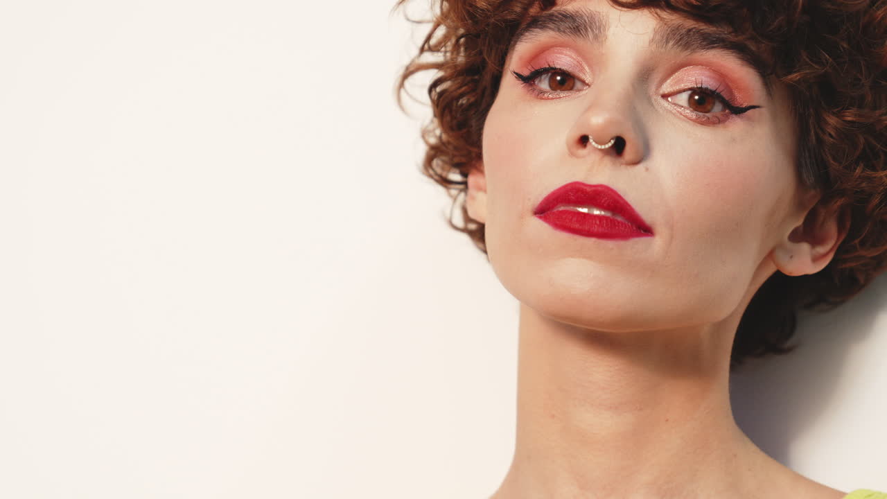 mujer despreocupada posando cerca de la pared blanca en el estudio con el peinado rizado