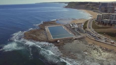 Aerial-drone-shot,-late-afternoon,-flying-south-along-the-coast-over-the-ocean-baths-and-Merewether-baths