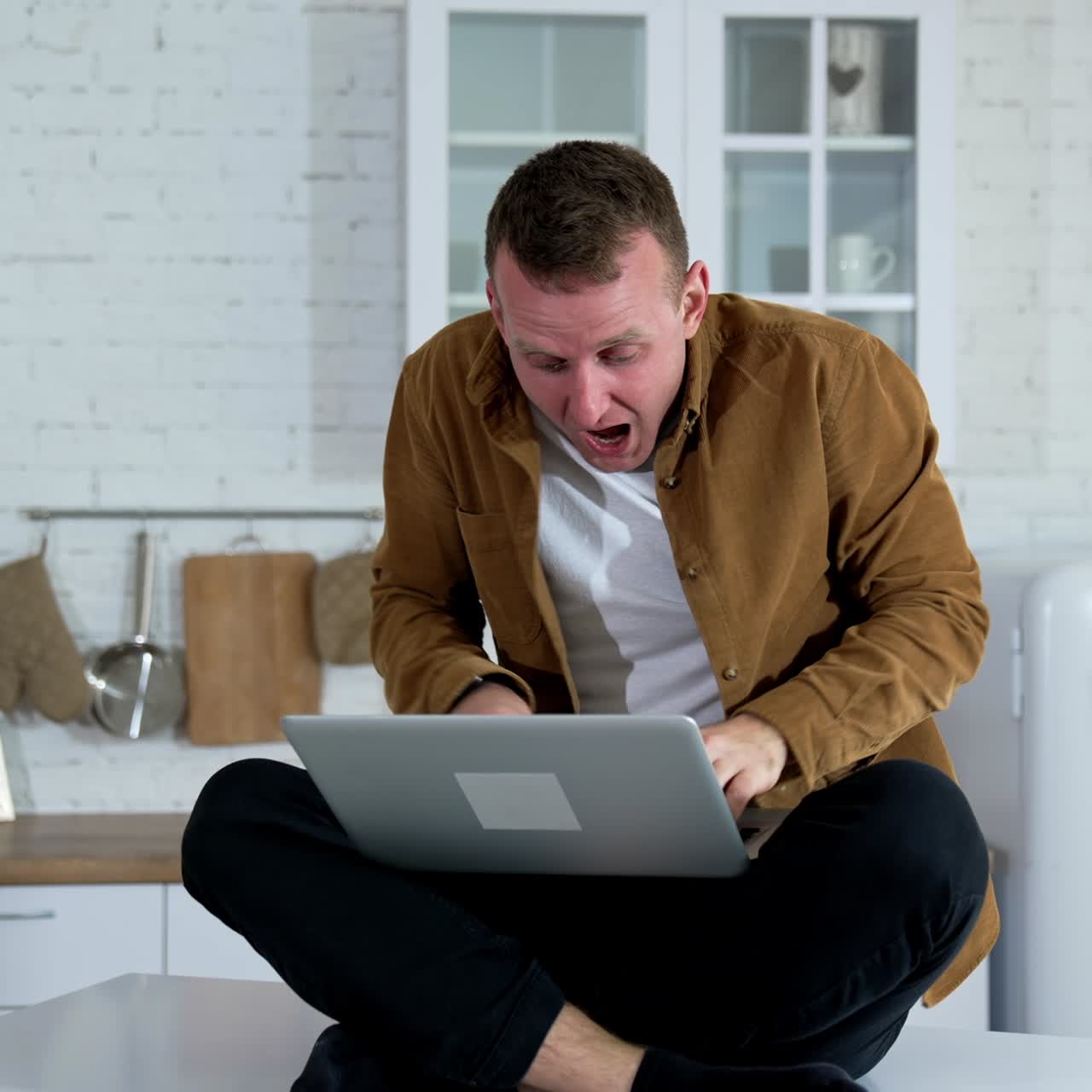 Emotional young man playing games at home. Funny man pointing with finger on camera while sitting on the kitchen table with a laptop