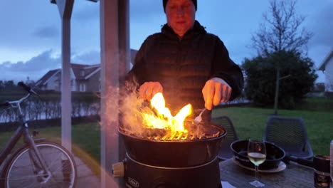 a man grills food on a barbecue in the evening, with flames rising from the grill