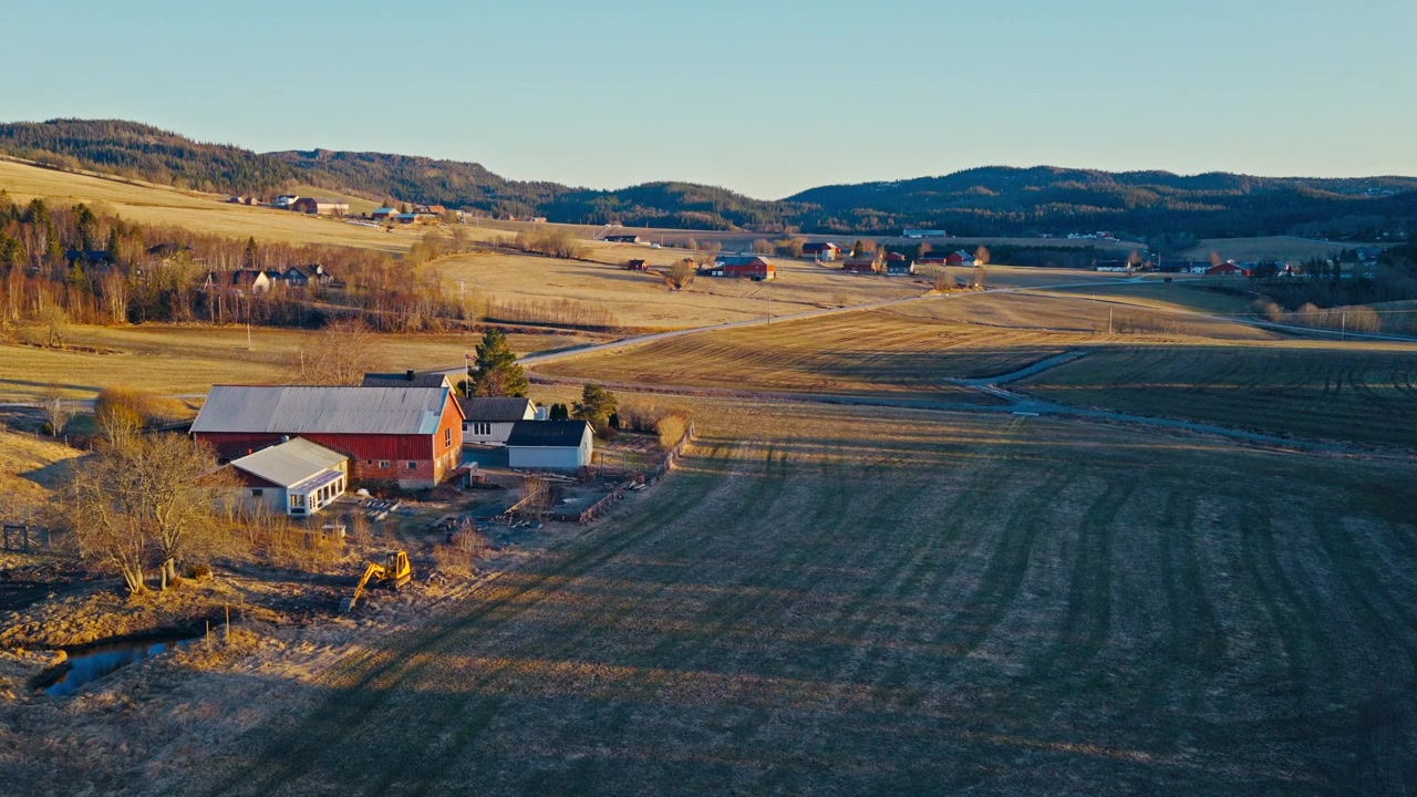 En lade og et stuehus i et landligt landskab i Norge, omgivet af åbent land og naturlig vegetation.
