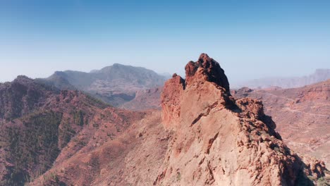 Aerial-Drone-tracking-across-and-down-dry-red-rocky-ridge-towards-mountain-valley-in-Gran-Canaria-Spain