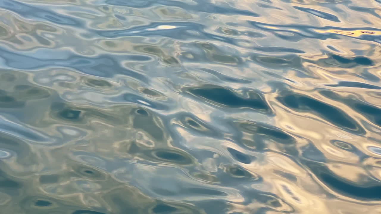 Superfície da água refletindo a luz durante o dia com ondas suaves e tons variados em um ambiente natural.