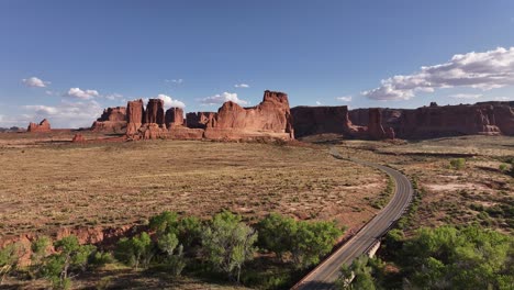 Aerial-view-of-a-road-winding-beneath-the-red-rock-formations-of-Utah's-desert-near-Moab,-USA,-highlighting-the-desolate-and-rugged-landscape