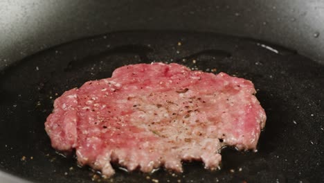 cooking a raw ground beef burger in a pan