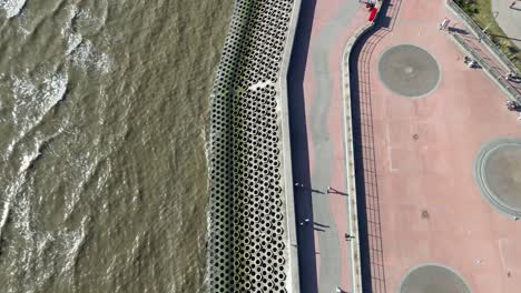 aerial drone flight along the coastline of blackpool looking down from above and slowly panning upwards to reveal the long coast and its piers with the tower in the distance