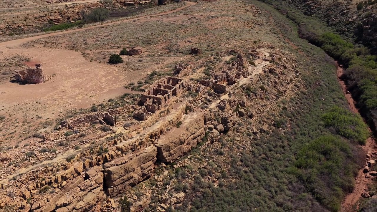 Een weids dronepanorama van zonovergoten woestijnruïnes die uitkijken over een diepe kloof. De ruige stenen muren en de uitgestrekte wildernishorizon creëren een krachtig beeld voor historische verhalen.